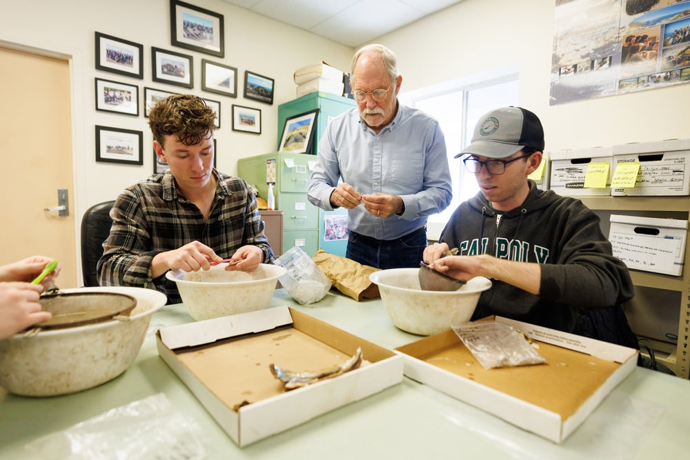 Two students and a faculty member examine artifacts in a lab