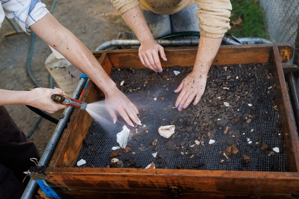 Two students touch dirt and water as they wetscreen artifacts