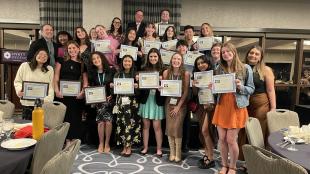 Students hold up paper certificates during an awards ceremony.